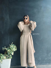 Woman wearing YEZWE Nomade Cey Jumpsuit with a hijab and sunglasses standing at glass door entrance confidently